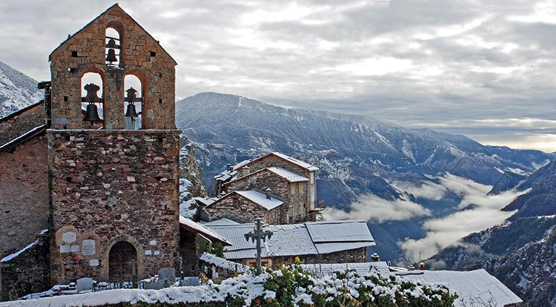 Le clocher et une façade de l'église de Roure avec, en arrière plan, la vallée de la Tinée